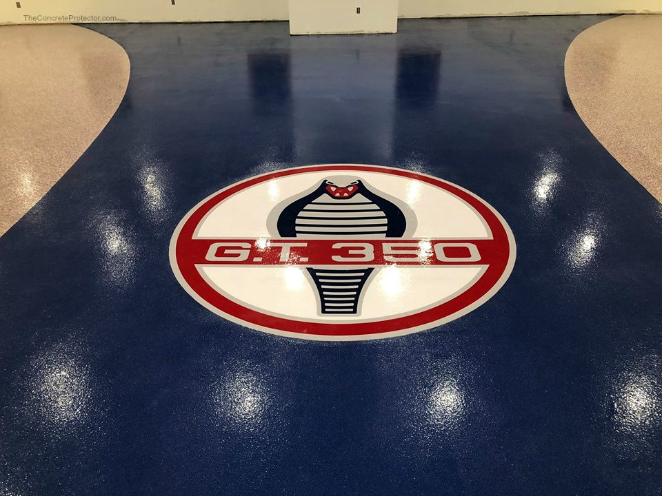 Custom concrete floor logo — Shelby GT350 cobra emblem sealed under epoxy in a navy blue garage floor