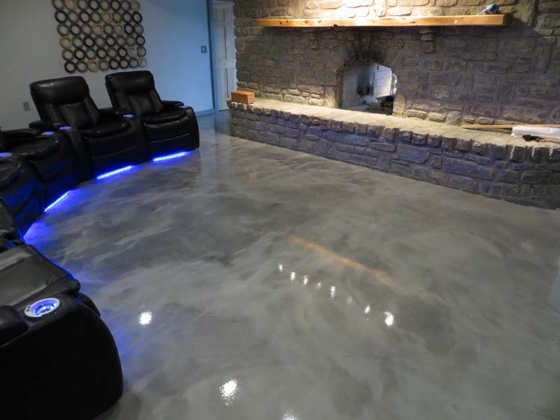 Metallic epoxy flooring in a home theater — silver and gray swirl effect with high-gloss finish reflecting LED lighting